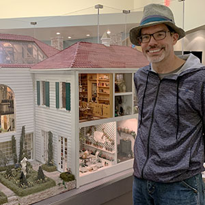 Paul Nylander standing beside a very large minature dollhouse